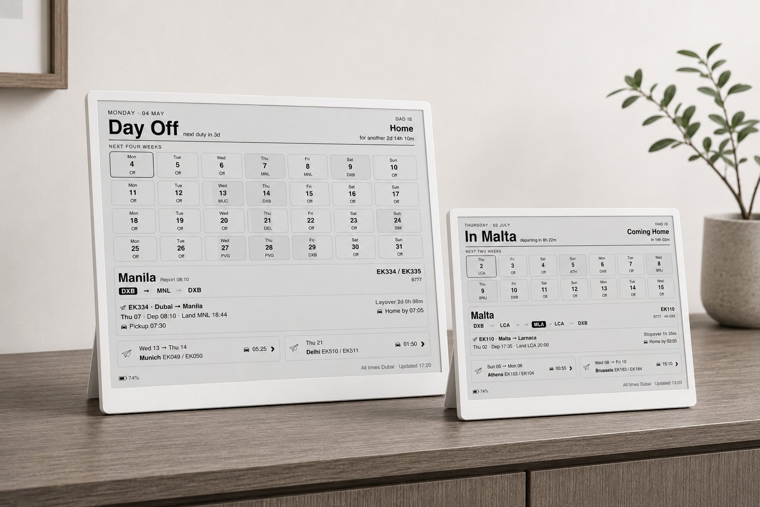 Two Roster Dashboard e-paper displays on a sideboard — the 10.3-inch four-week view and the 7.5-inch two-week view, both showing the same sample roster